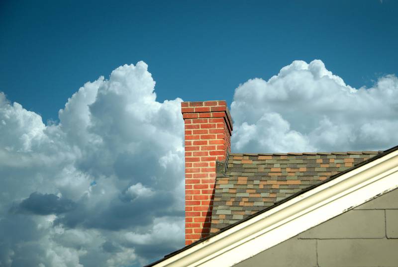 Chimney and roof with blue sky and clouds behind.