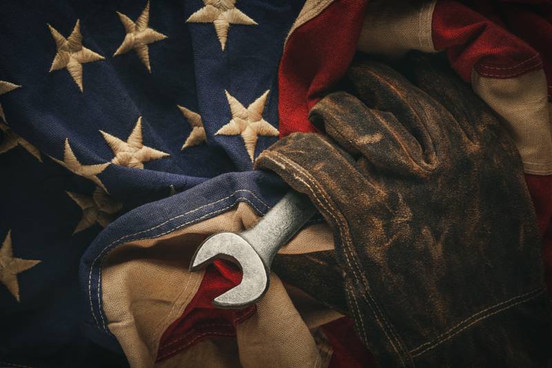 Worn work glove holding old wrench and US American flag. Made in USA, American workforce, blue collar worker, or Labor Day concept.