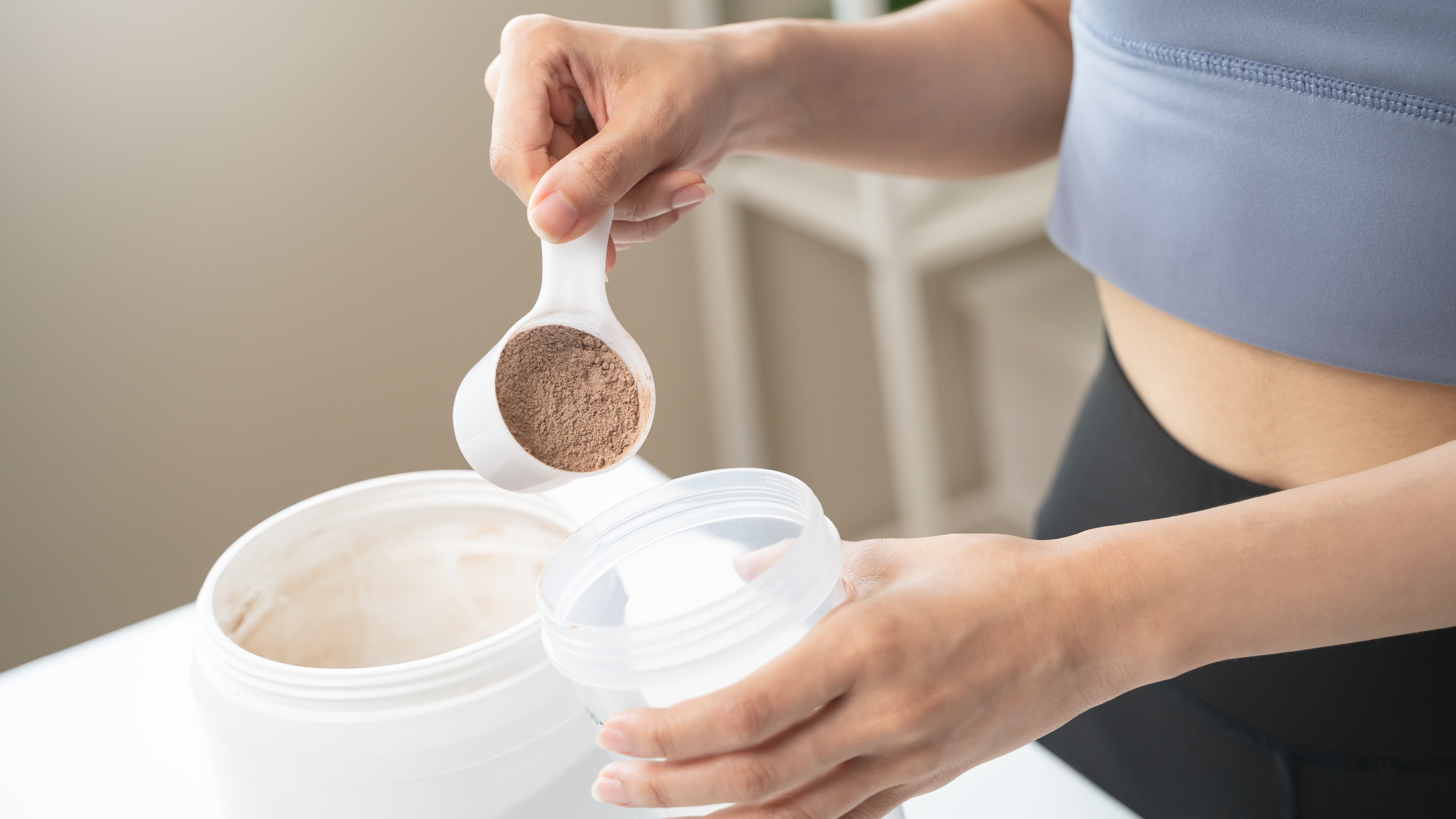 Young sporty woman pouring protein powder into a cup