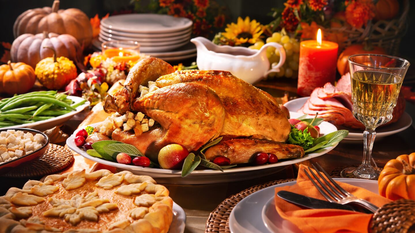 Thanksgiving dinner. Roasted turkey garnished with cranberries on a rustic style table decorated with pumpkins, vegetables, pie, flowers and candles