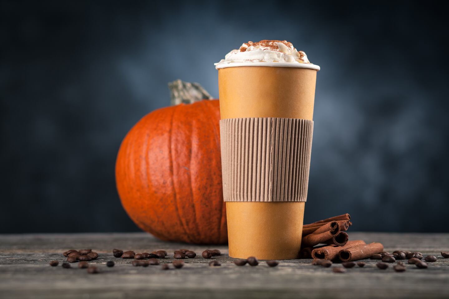 Pumpkin spice latte in a paper cup on dark background