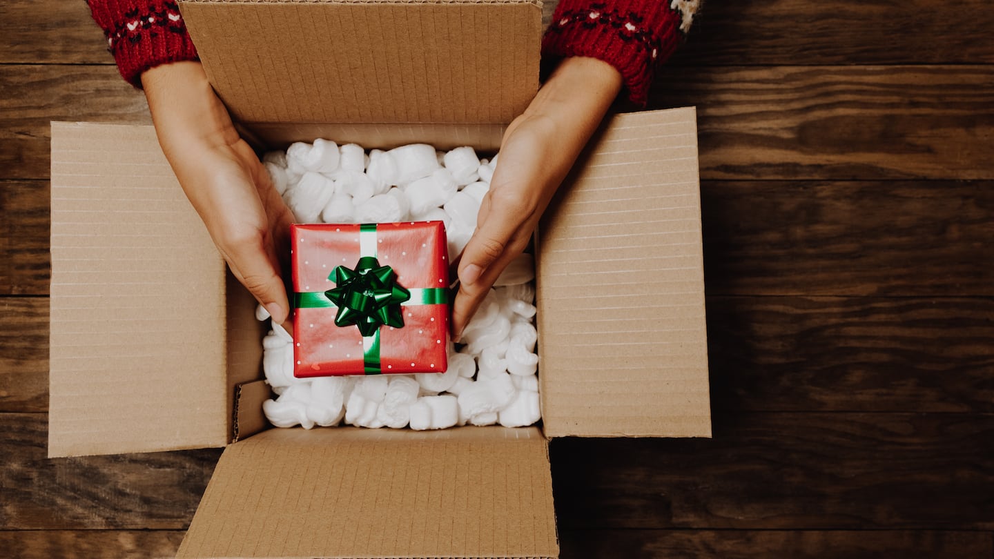 Female hands with a winter sweater packing or unpacking a Christmas gift from a cardboard box on a rustic wooden table.